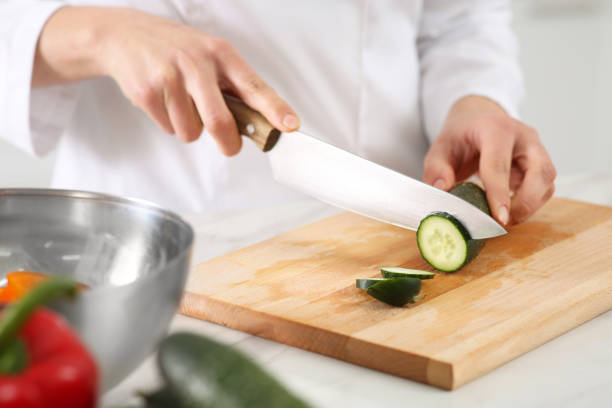 istock Professional chef cutting fresh cucumber at white table in kitchen, closeup 1466742437