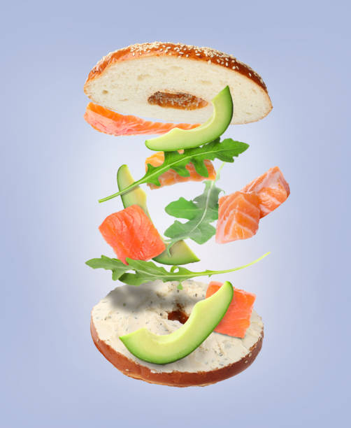 Tasty cut bagel with different ingredients flying on grey background Tasty cut bagel with different ingredients flying on grey background arugula falling stock pictures, royalty-free photos & images