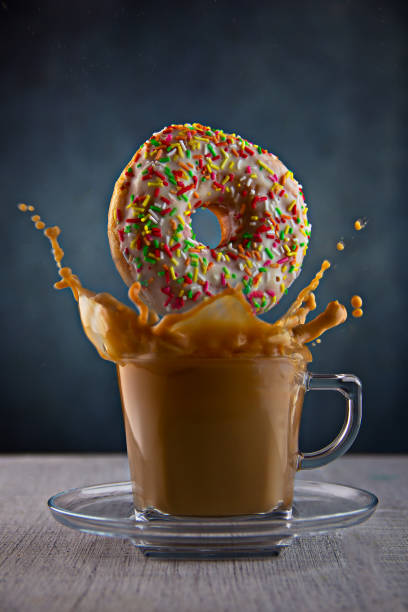 istock a donut with a multicolored icing crumb falls into a cup of coffee with milk 1466744655