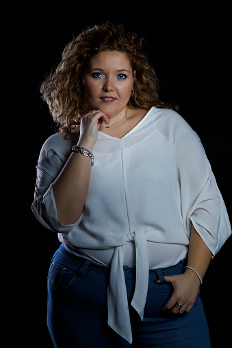 Plus size fashion model in denim clothes and white shirt on black background, overweight female body