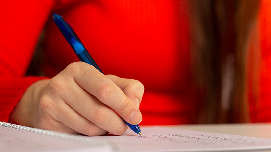 A girl at the table writes with a pen in a notebook. Student studying, taking notes. School and education. Closeup photo