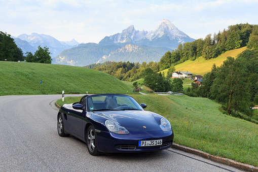 Fusch, Austria - July 25, 2021: Blue roadster Porsche Boxster 986 with mountain panorama at Grossglockner High Alpine Road. The car is a mid-engine two-seater sports car manufactured by Porsche.