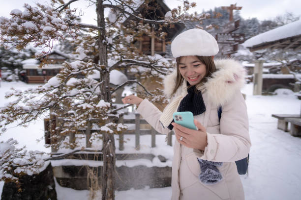 Beautiful woman tourists using phone and enjoying their trip to Japan in snow winter. stock photo