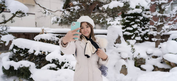 Beautiful woman tourists using phone and enjoying their trip to Japan in snow winter. stock photo