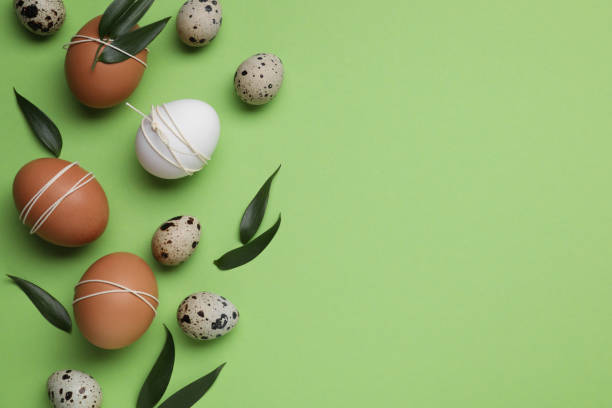 istock Beautifully decorated Easter eggs and leaves on light green background, flat lay. Space for text 1466751919