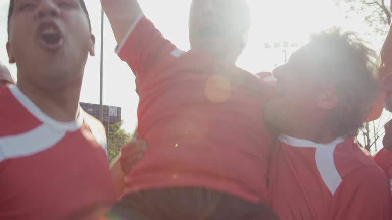 Happy middle-aged male football players carrying a teammate on their shoulders in celebration