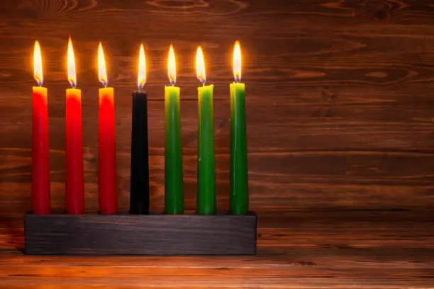 Photo of Kwanzaa festival concept with seven candles red, black and green in candlestick on wooden background, copy space