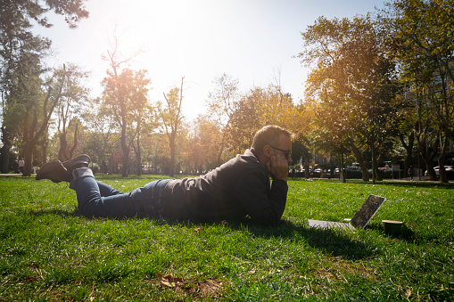 Man using laptop in city park lying on grass