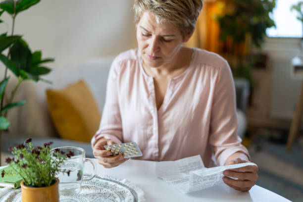 Holding blister pack with pills in hand and reading medical instructions A woman is looking at her pills and holding the leaflet information for her medication, sitting in her apartment oestrogen stock pictures, royalty-free photos & images