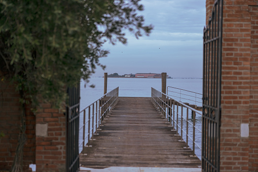 Diminishing perspective of empty pier leading towards Grand Canal and distant view of island against cloudy sky at Venice,Italy