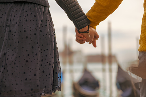 Midsection of loving couple holding hands in front of defocused gondolas moored at Grand Canal while exploring Venice in Italy