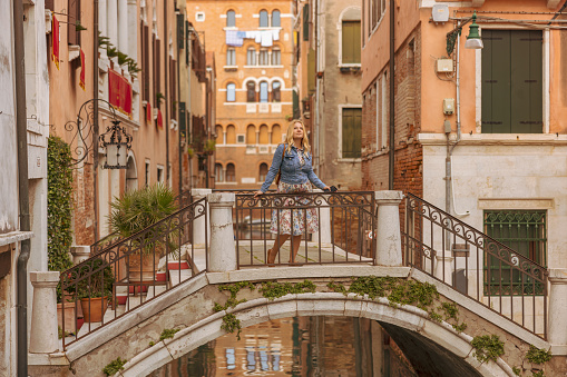 Female tourist standing on arch footbridge against historic residential buildings while enjoying vacation in Venice,Italy