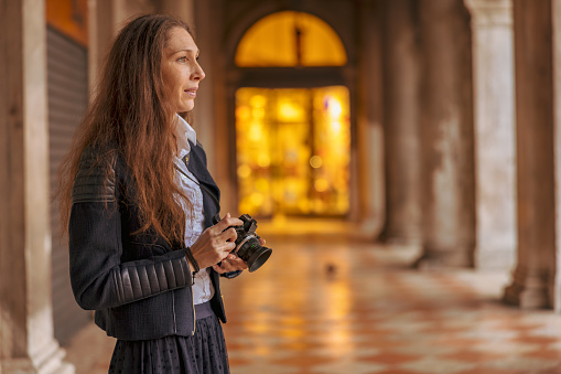 Side view of mid adult female tourist with camera looking away while standing in Procuratie Vecchie at Venice,Italy during vacation