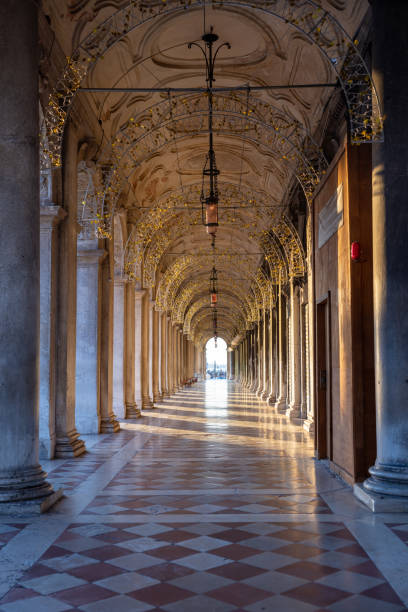 Diminishing perspective of empty archway with colonnade and lighting equipment hanging on ceiling in Procuratie Vecchie at Venice,Italy