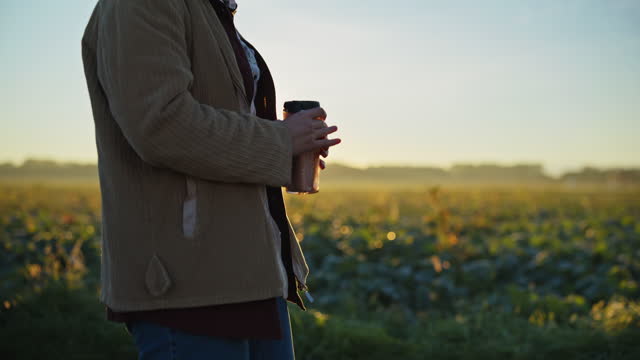 Female farmer with coffee walking toward car in sunrise field