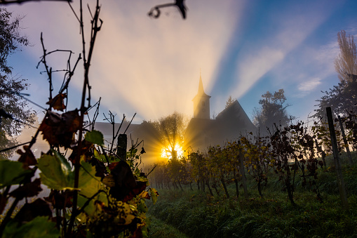 Beautiful view of sunshine through silhouette Church of the Sorrowful Mother of God against dramatic sky seen through vineyard during sunrise