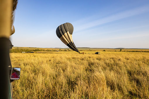 Deflated hot air balloon falling on grassy landscape against sky at Maasai Mara National Reserve during sunny day in Kenya,East Africa
