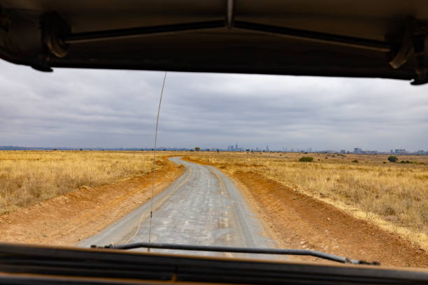 Diminishing perspective of empty road passing through grassy landscape against cloudy sky during sunny day in Kenya,East Africa seen though car windshield