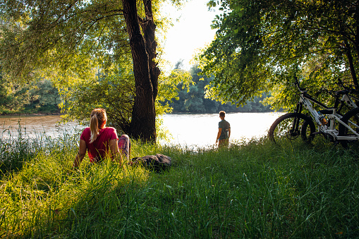 Couple with bicycles relaxing along riverside in green forest during summer