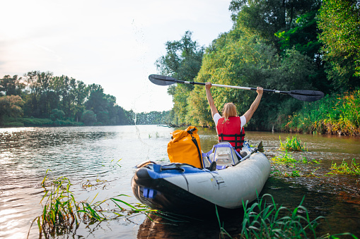 Woman with arms raised holding oar while sitting in kayak on river during summer