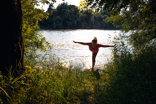 Woman practicing yoga at river bank in forest during summer