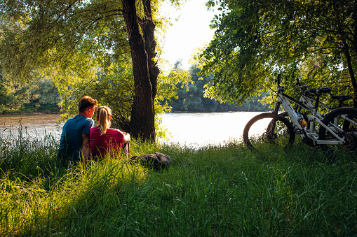 Couple with bicycles sitting by river in green forest during summer