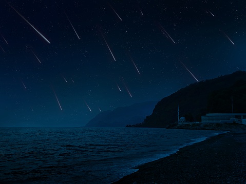 Meteor shower in the sky over the sea. Falling meteorites at night over the beach and seashore. Beautiful landscape with shooting stars.