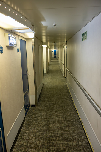 Empty illuminated white corridor with doorways and closed door in ferry