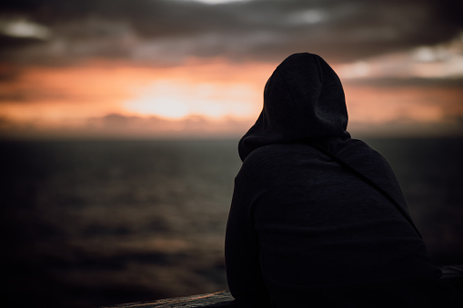 Rear view of woman wearing hooded jacket looking at sunset view while traveling in cruise during vacation