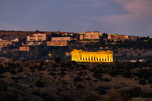 Illuminated Temple of Concordia with buildings on mountain in front of sky at dusk