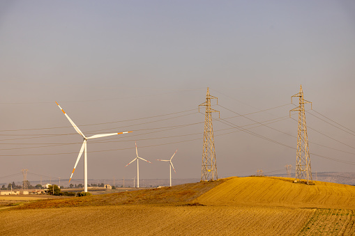Wind turbines and pylons with clear sky in background during sunny day