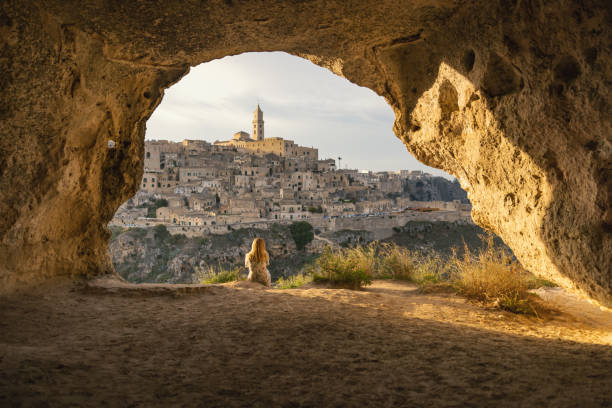 female tourist looking at cityscape while sitting at cave. matera - italy - women rear view one person arch imagens e fotografias de stock