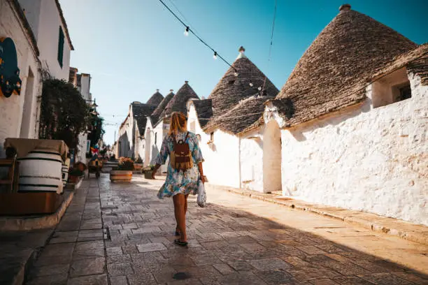 Tourist with backpack walking in alley amidst trulli houses in town