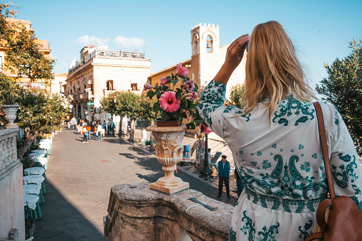 Rear view of female tourist standing by flowering plant in front of church in city during vacation