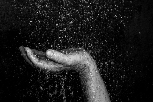 human hand in the rain against black background
