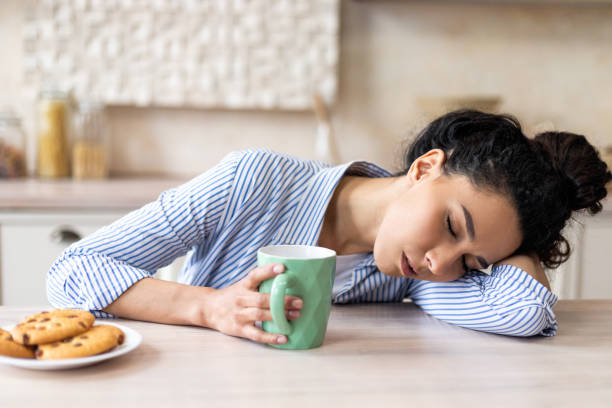 istock Tired latin woman with coffee cup, waking up early and sleeping on table in light kitchen interior, free space 1466775687