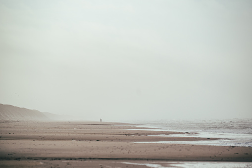 a person is walking in the distance on the stormy beach of the North Sea