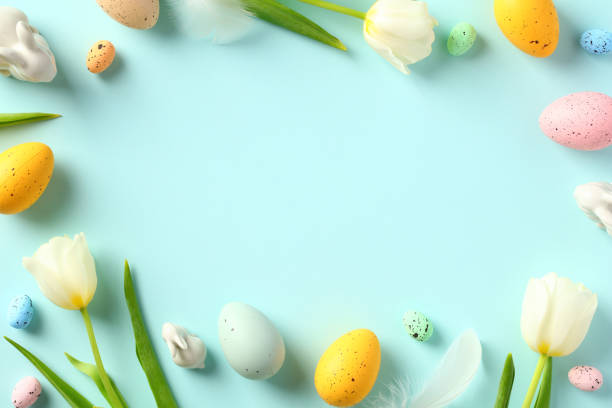 istock Happy Easter greeting card design. Frame made of tulips spring flowers, rabbit decorations, colorful Easter eggs on pastel blue background. 1466777890