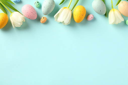 istock Happy Easter concept. Frame top border made of tulips spring flowers and colorful Easter eggs on light blue background. 1466778028