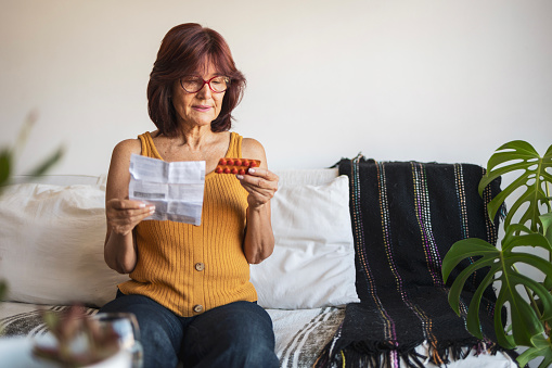 Latin woman using products for hormone replacement therapy. She is sitting on bed and reading patient information leaflet.