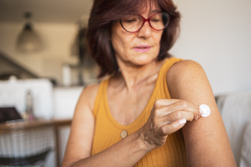 A woman in menopause sticks a transdermal patch on the skin. Hormone replacement therapy in menopause concept