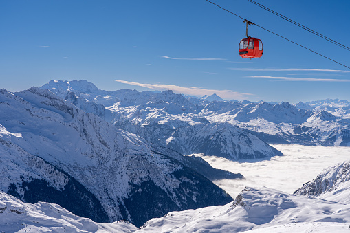 Red gondola of cable car seen from Bellecote glacier, La Plagne ski resort, France,  in winter. Inversion clouds in valley