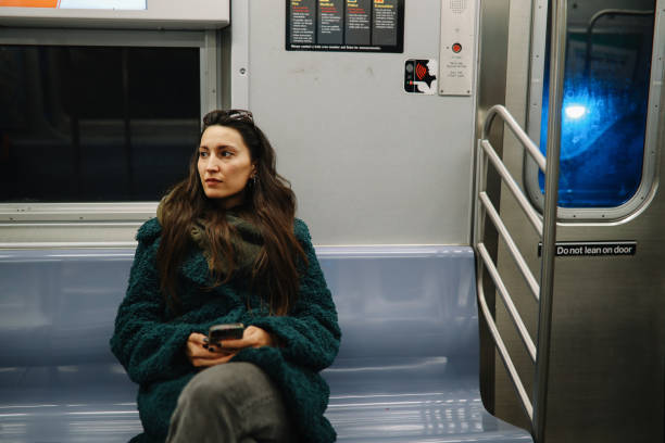 Woman in her 30s commuting through the streets of Manhattan, New York City. She is wearing a fake fur coat, on a sunny but cold winter day, checking messages on her smartphone while using the NYC subway.