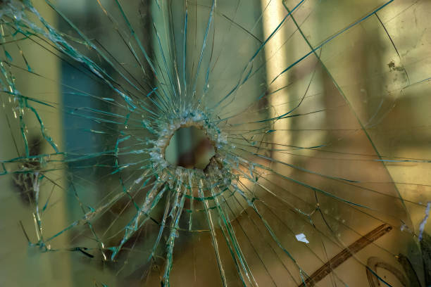 A hole in the window glass with a bullet during a military shooting. Cracks propagate around the hole. Dirty window frame. View of the street from the inside. stock photo