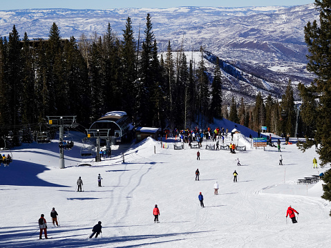 View of Colorado, USA, ski slope descending to resort town in winter; distant mountains and blue sky in background; view from the top of the slope