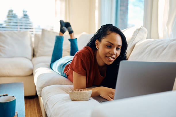 istock Happy black woman using laptop while relaxing on the sofa at home. 1466797150