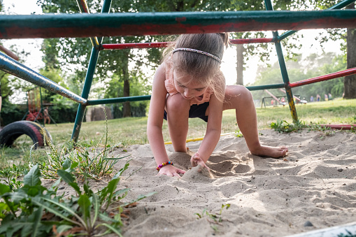 a little cute girl is playing with  sand on the playgraund