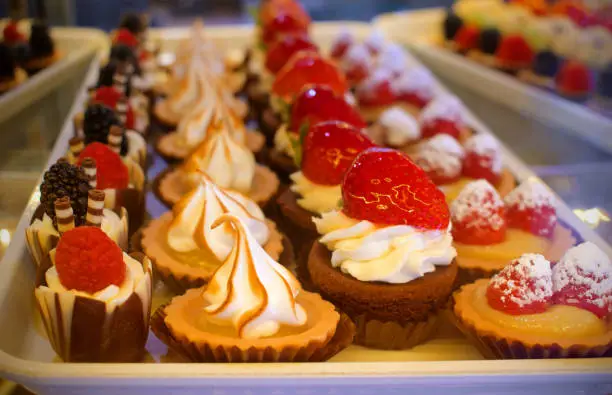 Photo of tray of delicious bite sized pastery confections topped with cream strawberry and rasberry fruit in a bakery window