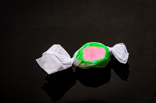A single piece of old fashioned green and pink salt water taffy on a black shiny background