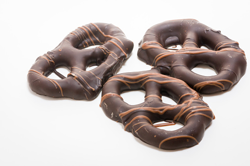 A grouping of three pretzels coated with dark  chocolate on a white background.